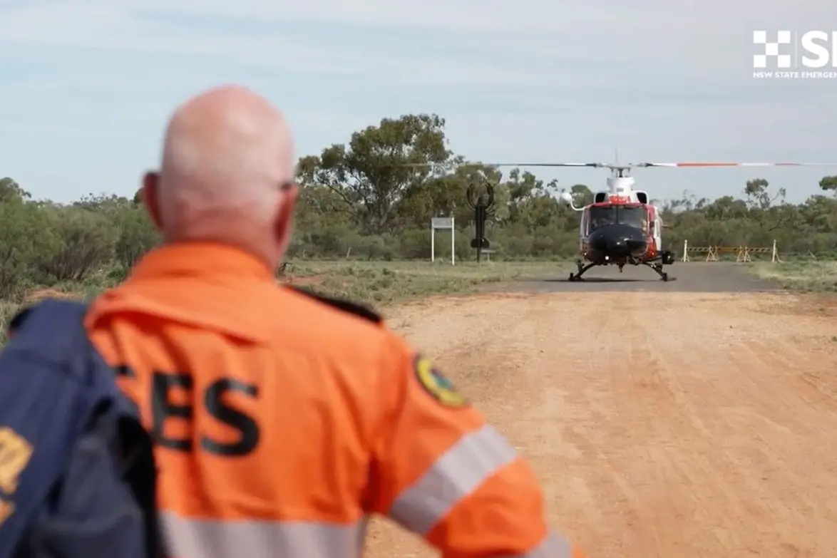 An SES crew member and helicopter are pictured during an operation in the Wanaaring area where floodwaters surpassed the 1990 record height, isolating residents across a broad catchment area. Photo: Supplied.
